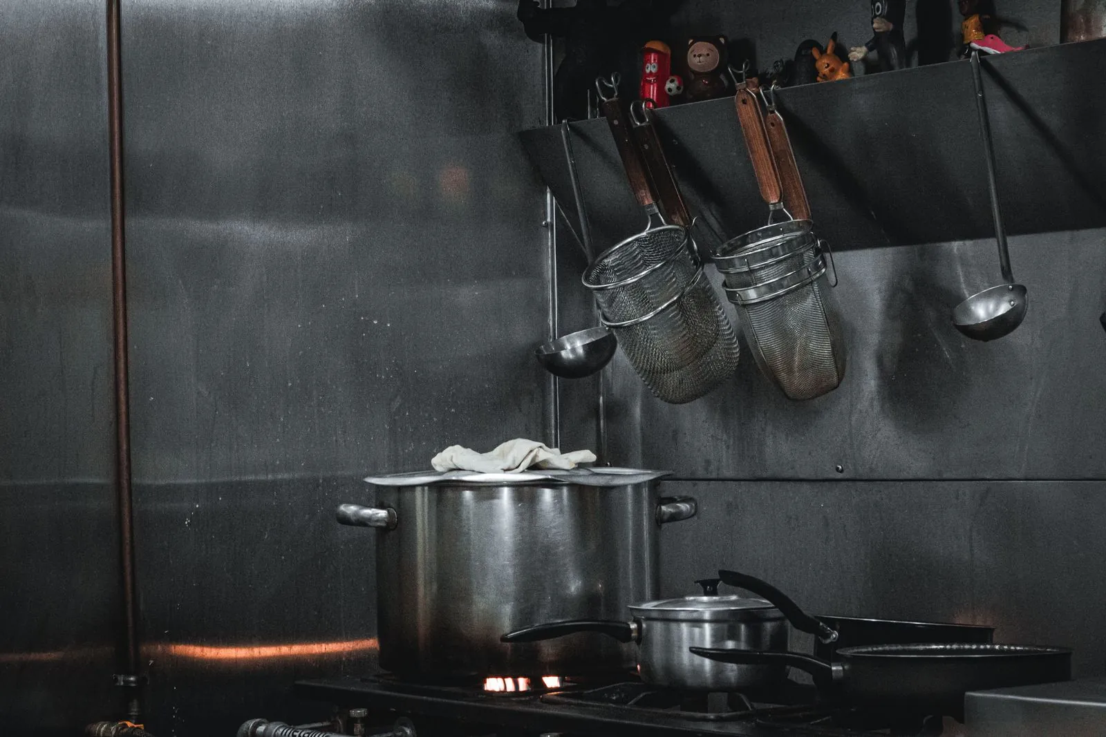 Stainless stockpots on a gas range under a rail of hanging utensils in a commercial kitchen