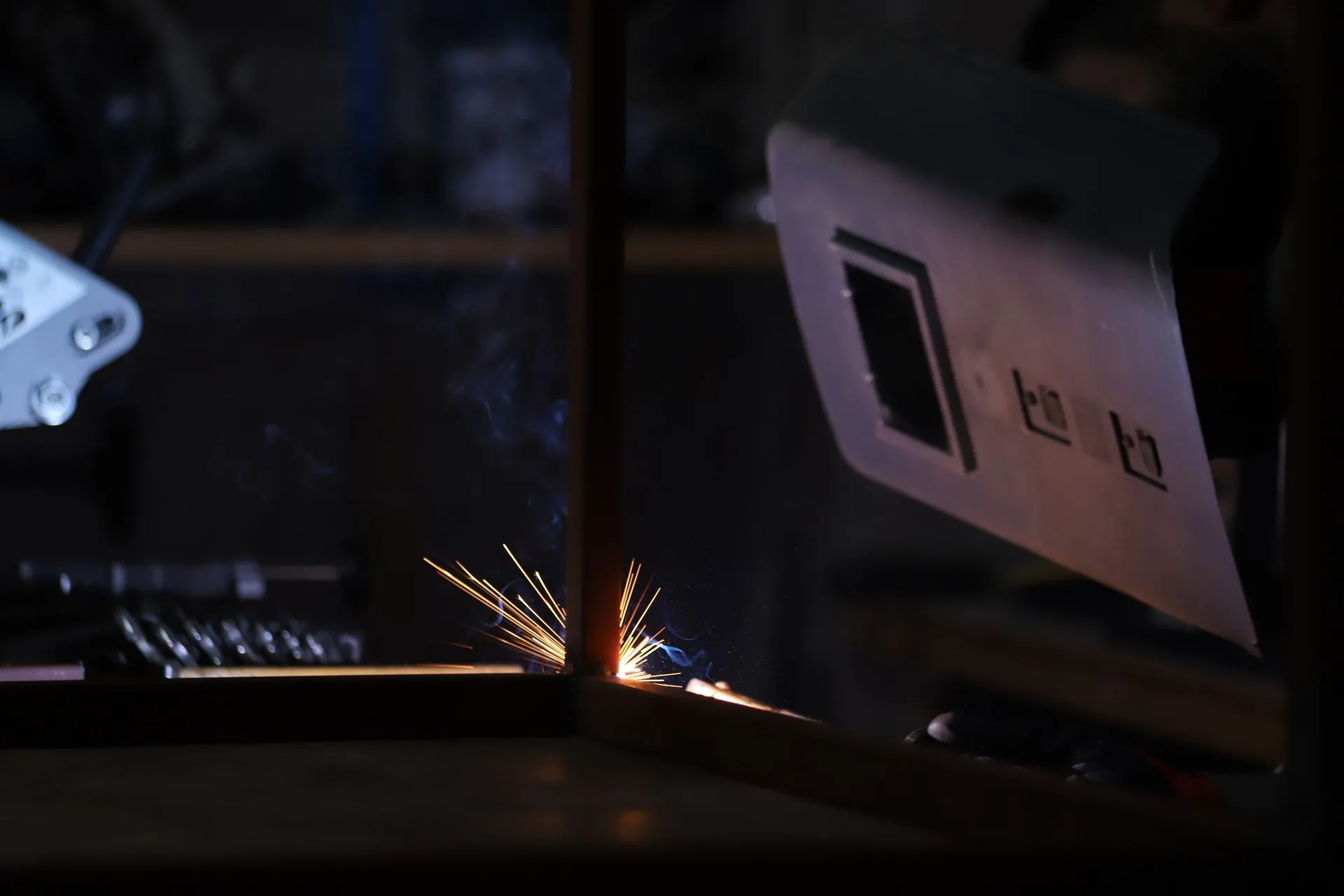 Sparks scattering from a weld on a steel panel in a dark fabrication workshop