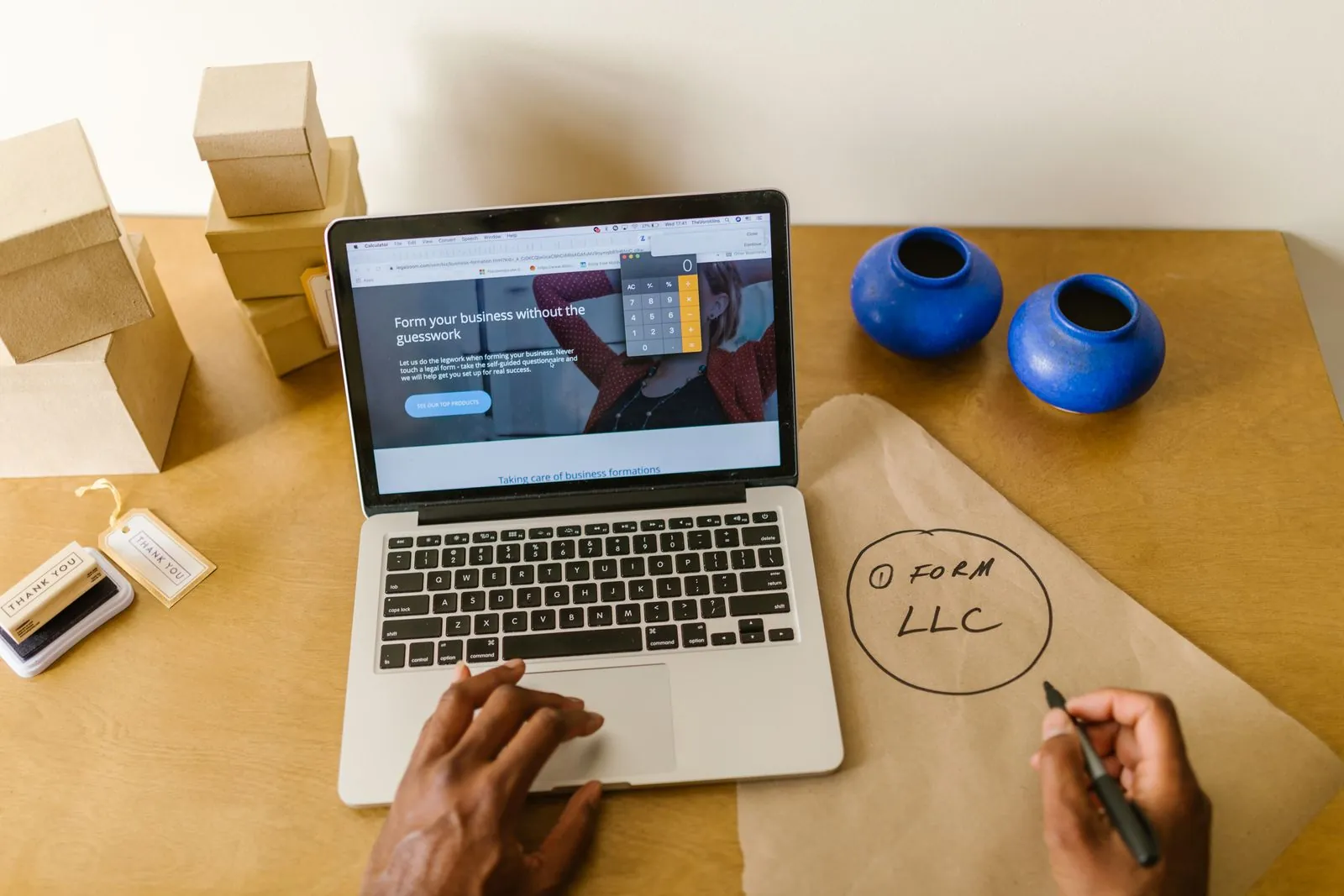 A business owner writing notes on an envelope beside a laptop and packed boxes at a desk