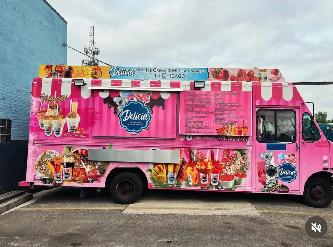 A finished food truck in a full-color pink wrap advertising ice cream and Mexican snacks, parked outside with its serving hatch closed and menu boards down the side.